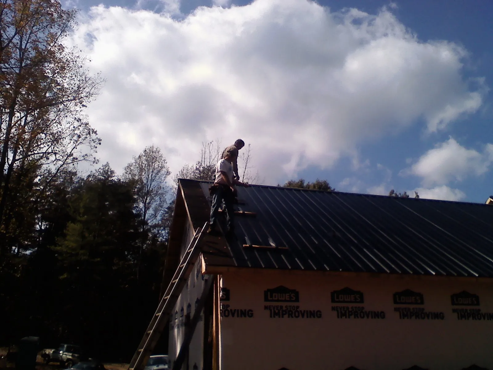 Roofer fastening dark metal panels high against a cloudy sky, from a Roof Inspection job in Oakdale